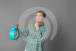 Freestyle. Boy standing isolated on grey wall with alarm clock looking up pensive