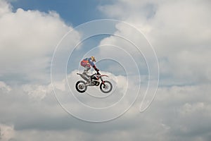 Freestyle Motocross rider carries out a trick with the motorcycle on background of the blue cloud sky. Extreme sport. German-Stunt