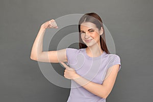 Freestyle. Young girl standing isolated on grey showing arm muscle smiling confident close-up