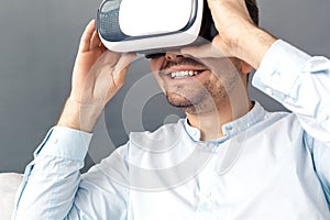 Freestyle. Young man looking through virtual reality headset studio sitting on sofa isolated on grey smiling excited