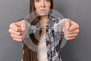 Freestyle. Young woman in cuffs standing studio isolated on grey close-up blurred background scared