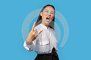 Freestyle. Young woman wearing shirt and skirt standing  on blue showing rock gesture grimacing cool