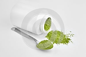 Freeze dried young organic wheatgrass powder in teaspoon and jar on white