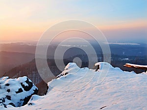 Freeze fallen trunk covered with fresh powder snow, stony rock peak increased from foggy valley. Winter misty sunrise in rocks.