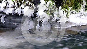 Freeze snowy big boulder in clear cold water of mountain river. Small icicles glitter above crystal water of noisy stream.