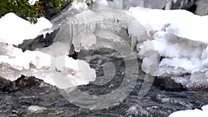 Freeze snowy big boulder in clear cold water of mountain river. Small icicles glitter above crystal water of noisy stream.