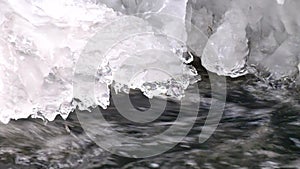 Freeze snowy big boulder in clear cold water of mountain river. Small icicles glitter above crystal water of noisy stream.