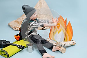 Freezing boy sitting next to a fake campfire, getting warm over blue background
