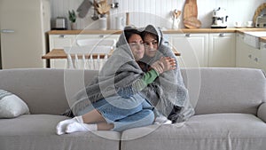 Freezing Caucasian woman and teen girl are sits on couch wrapped in plaid due to non-working heating