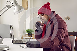 Freezing man sitting at desk blowing in his hands trying to keep warm
