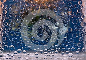 Freezing raindrops are located against the background of a window glass with green, cyan and gold highlights reflected in it.