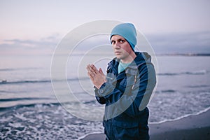 Freezing young man on the beach. Man feels freeze rubs and warms her hands.