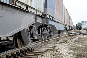 Freight cars with a wheelset node close-up going into the distance with the tanks of another train in the distance