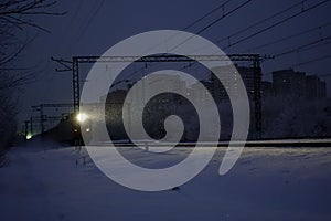 Freight train at night. The headlights and locomotive headlights illuminate the falling snow. Russia