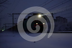 Freight train at night. The headlights and locomotive headlights illuminate the falling snow. Russia