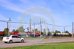 Freight train on railway and car moves on road near green grass