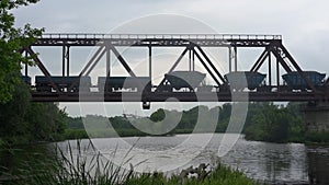 Freight train rides on a railway bridge over the river