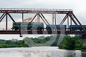 Freight train rides on a railway bridge over the river