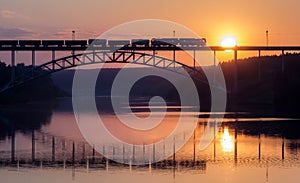 Freight train rides on the railway bridge over the river during sunse