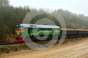 Freight train transports sand with freight wagons in a sand pit in cloudy foggy weather.