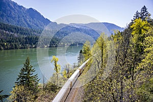 Freight train travels by rail along the Columbia River with a ridge of mountains on the opposite bank of the Columbia Gorge