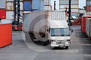 Freight trucks, container boxes in logistic shipping yard with stacks of cargo containers in the background