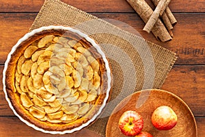 French apple tart aside Gala apples and cinnamon sticks on natural rope mat on a vintage wood table. Flat lay. Top view