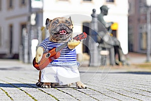 French Bulldog dog dressed up as street perfomer musician wearing a funny costume with shirt and arms holding a toy guitar