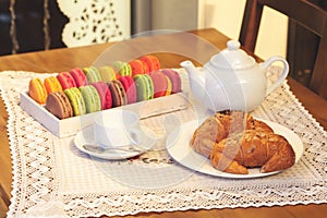 French colorful macarons in a box, croissants, cup and teapot