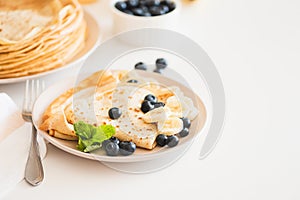 French crepes with banana and blueberries on white table. Copy space