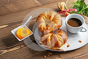 French croissants, cup of coffee and peach jam on the wooden table. Tasty breakfast with coffee and croissant with ham and cheese