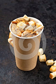 French cuisine hot food delivery - Close-up of mushroom soup with chicken meat in disposable paper cups on a dark stone