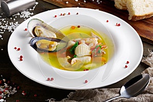 French seafood soup with white fish, shrimps and mussels in plate at wooden background