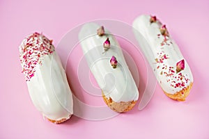 French dessert eclairs or profiteroles with rose-flavored white chocolate glaze, on a pink background. Pastry cakes with custard,