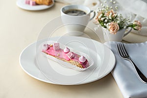 French desserts eclairs with pink icing and cup of coffee on the table