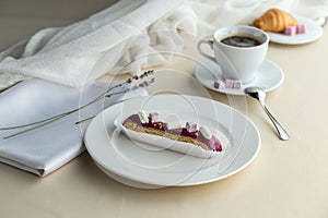 French desserts eclairs with violet icing and cup of coffee on the table
