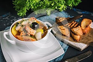 French fish soup Bouillabaisse with seafood, salmon fillet, shrimp, rich flavor, delicious dinner in a white beautiful