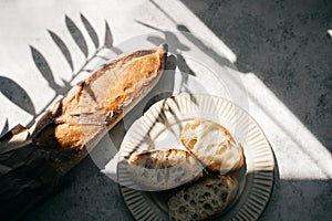 French fresh bread baguette with slices on a ceramic plate on gray background.