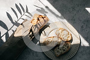 French fresh bread baguette with slices on a ceramic plate on gray background.