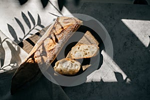 French fresh bread baguette with slices on a ceramic plate on gray background.