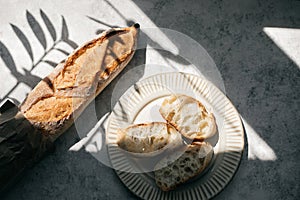 French fresh bread baguette with slices on a ceramic plate on gray background.