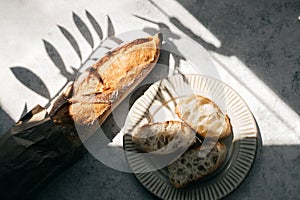 French fresh bread baguette with slices on a ceramic plate on gray background.