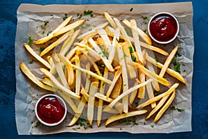 French fries arranged on baking paper with ketchup and herbs