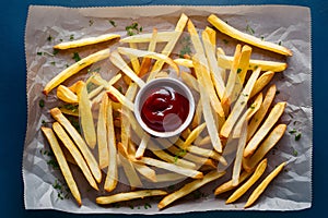 French fries arranged on baking paper with ketchup and herbs