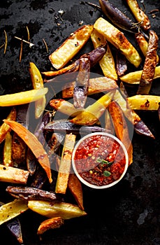 French fries, baked fries from different types and colors of potatoes sprinkled with herbs and spices with spicy tomato sauce