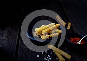 French fries on a black saucer, red sauce and spoon on dark wooden background