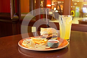 French fries and burger with a knife stuck in the middle- cheese, sausage in a grunge plate,piano with ketchup sauce, with a glass