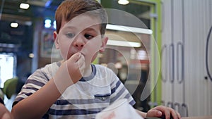French fries and burger for lunch for schoolboy, male child eats hamburger and french fries with sauce in fast food cafe