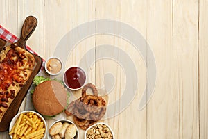 French fries, burger and other fast food on wooden table, flat lay with space for text