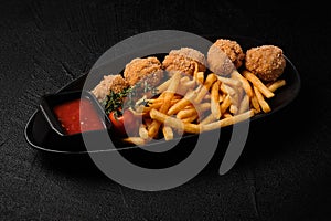 French fries and cheese balls served on a black background
